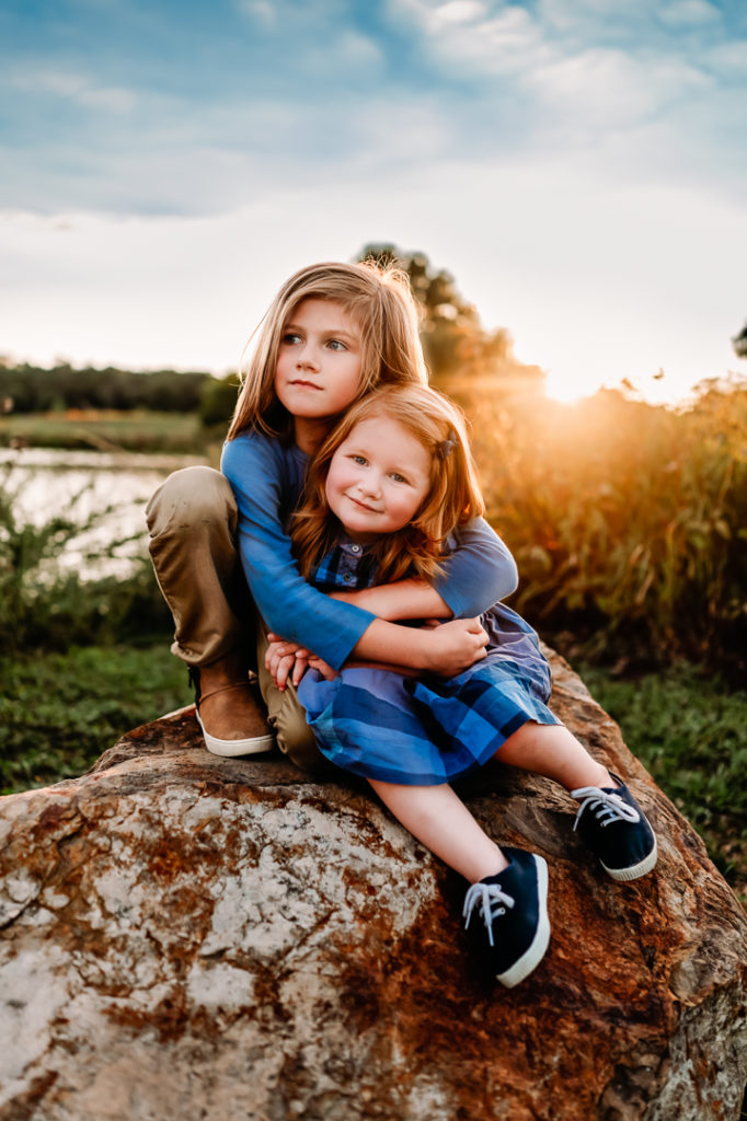 sister and brother sitting on a rock at sunset